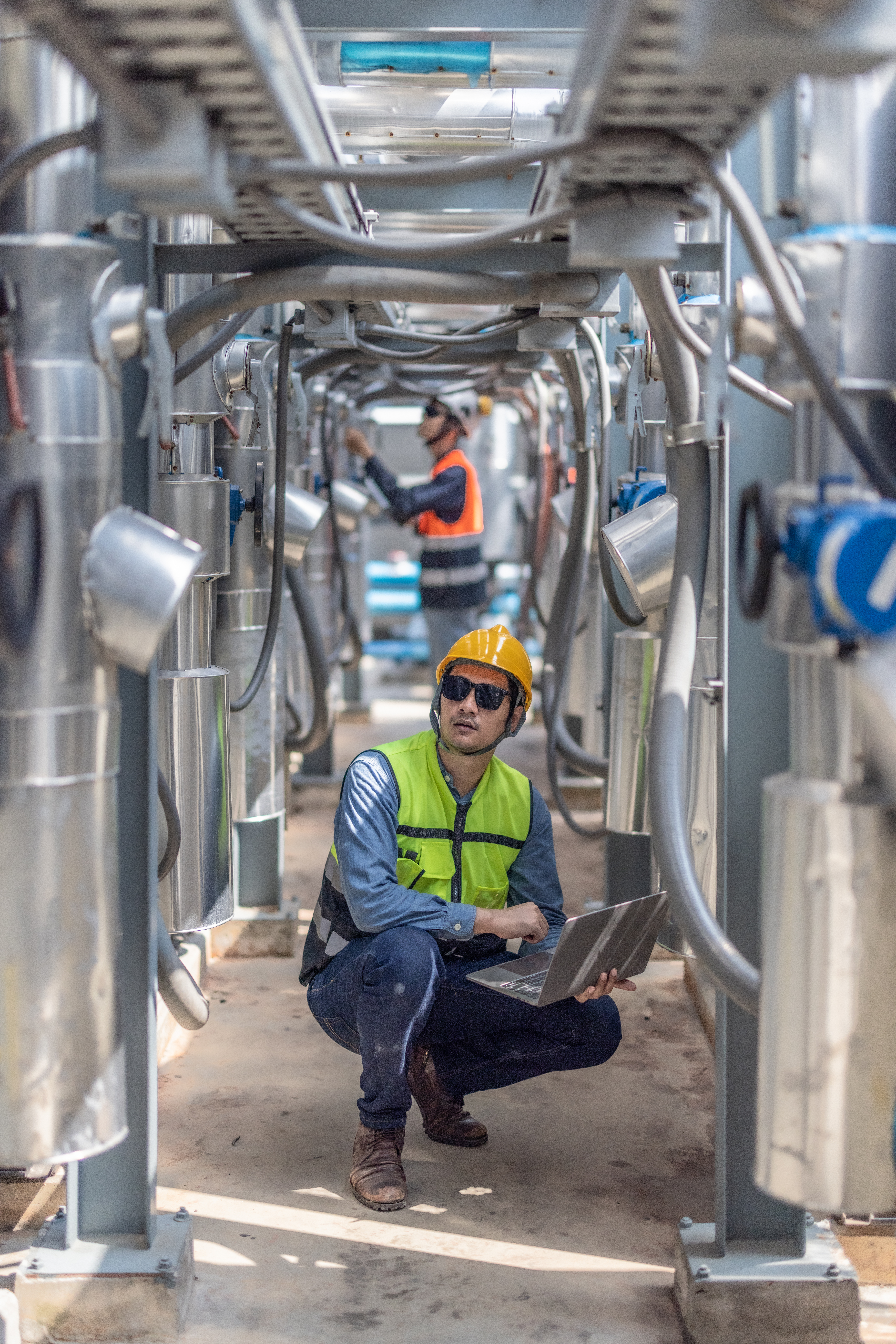 Professional industrial engineer, equipped with a laptop, meticulously troubleshooting an HVAC system within the complex pipeline infrastructure of a modern facility. Reducing carbon footprint.